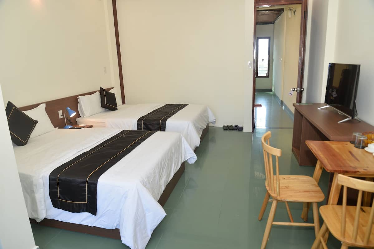A hotel room with two beds, a desk with chairs, a television, and a hallway leading to another room.