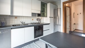 A modern kitchen with white cabinets, a stainless steel sink, a built-in oven, and a refrigerator.