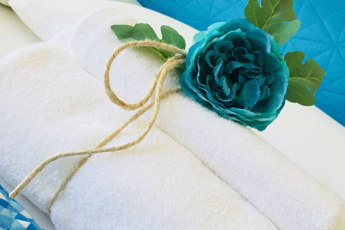 A neatly folded white towel tied with a string and a blue rose decoration on a bed with patterned bedding.