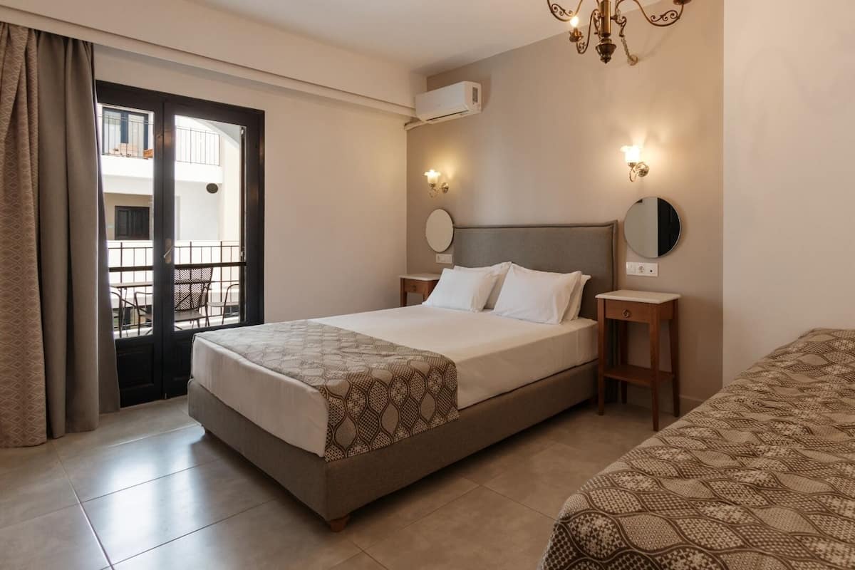 Habitación de hotel con cama, mesita de noche, espejo y balcón con una silla.
