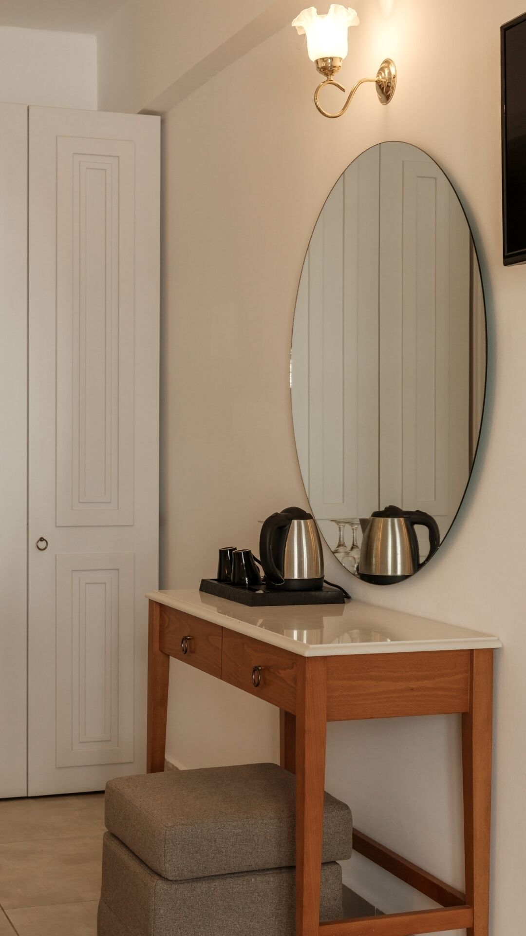 A small, neatly organized room with a wooden table, a mirror, and a kettle.