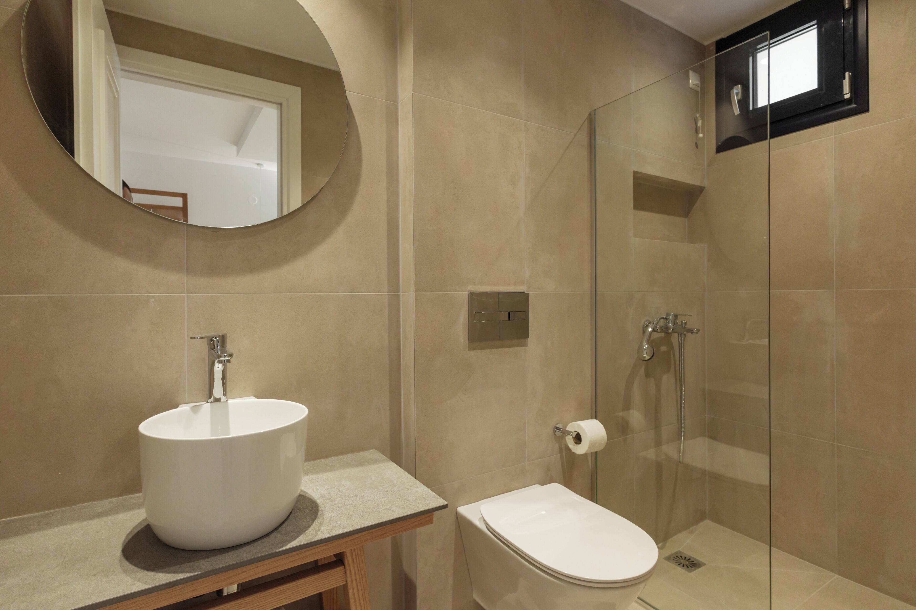 A bathroom with a round mirror, a white sink, a toilet, and a glass-enclosed shower.