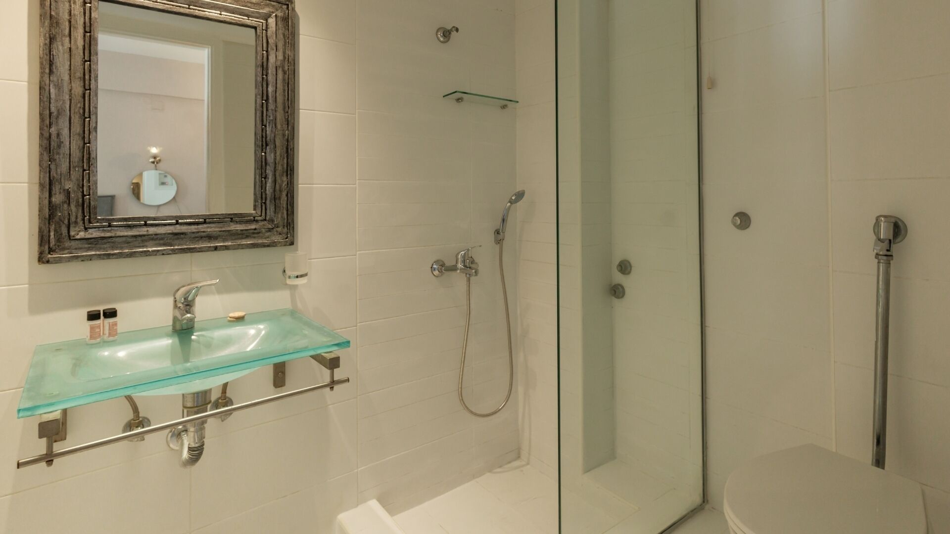A bathroom with a glass sink, a mirror, a shower, and a toilet.