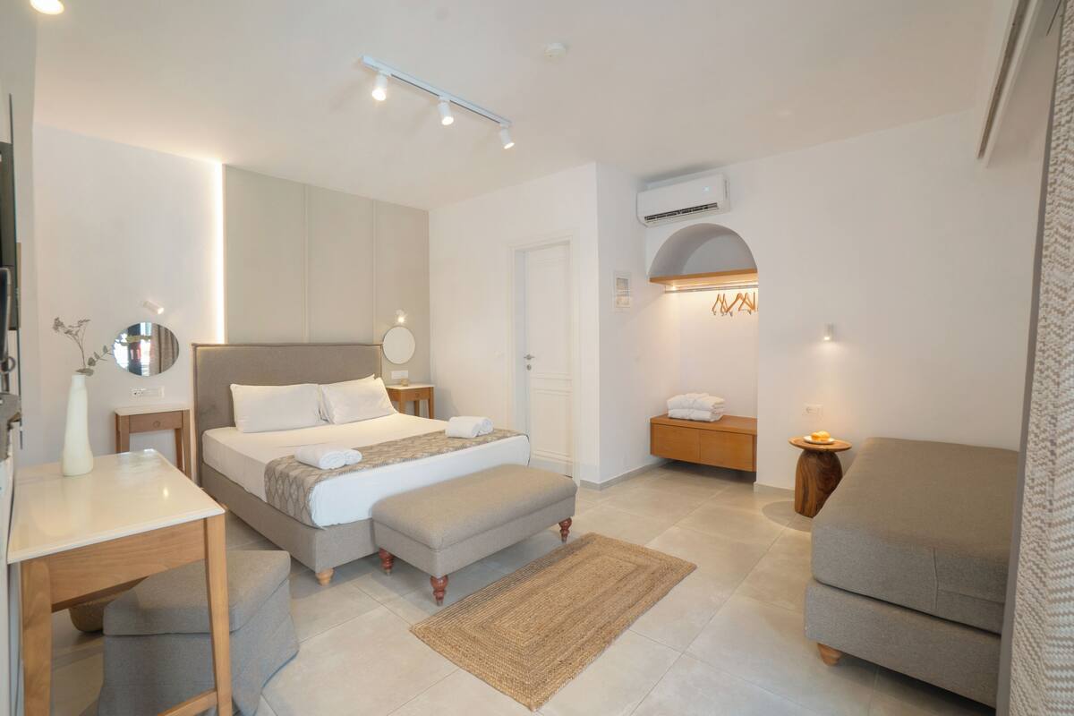 Un dormitorio moderno con cama, mesitas de noche, escritorio, banco, sofá y aire acondicionado.