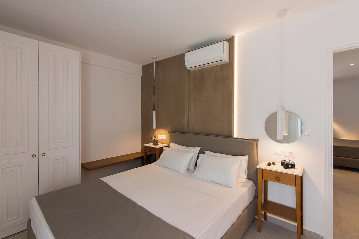 Habitación de hotel con cama, mesita de noche, lámpara, equipo de aire acondicionado y espejo.