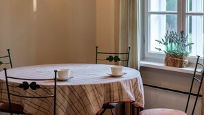 Un comedor con una mesa redonda, cuatro sillas, una lámpara de pared, un ventanal con cortinas y una planta en el alféizar.