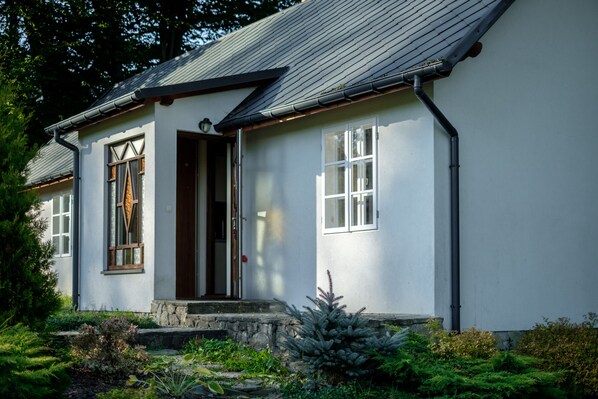 A white building with a stone foundation, a wooden door, and a window with a wooden frame.