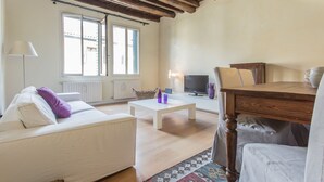 A living room with a white sofa, a wooden coffee table, a TV, and a window with blinds. - Padova - Via Tadi 39 (Padova)