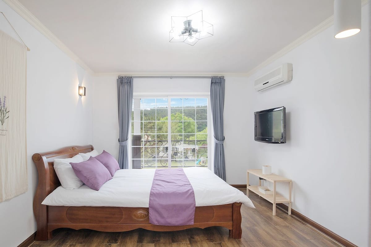 A bedroom with a wooden bed, a window with a view, a flat-screen TV, and a ceiling light.