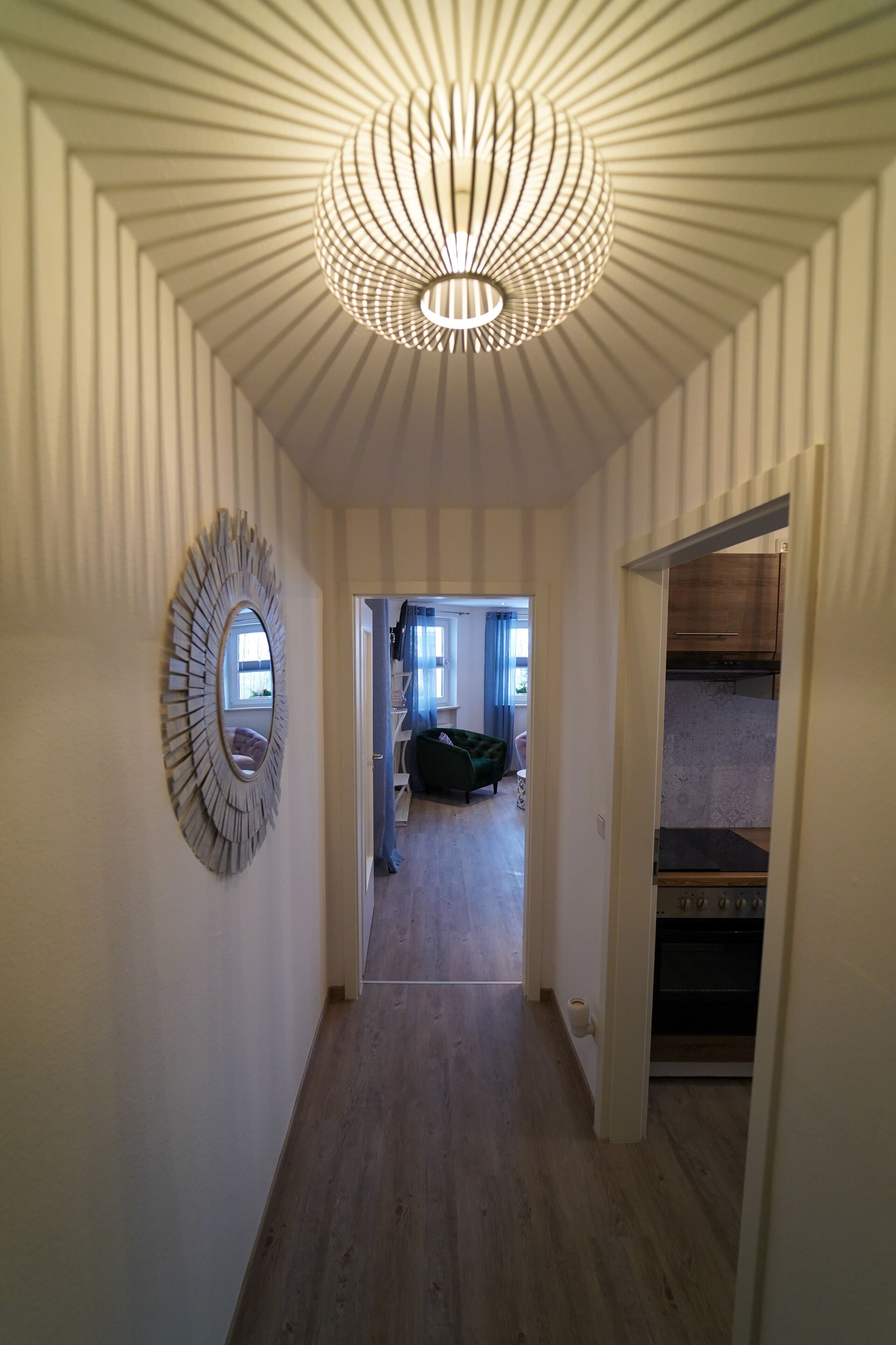 Un couloir doté d’un plancher en bois, d’un luminaire au plafond et d’un miroir accroché au mur.