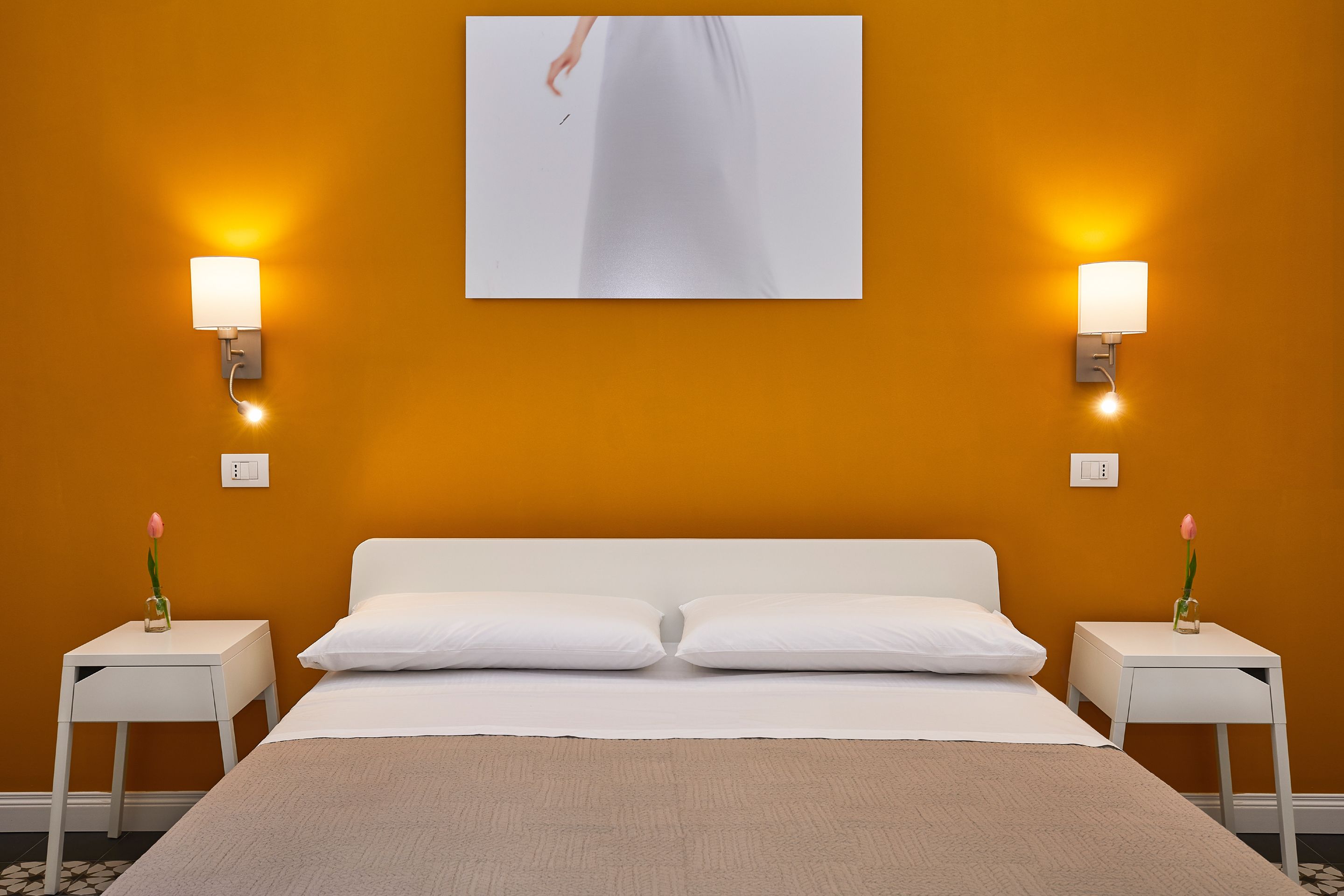 A hotel room with a bed, two bedside tables, and wall-mounted lamps.