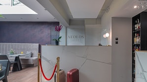 Zona de recepción con pared de mármol, mostrador de recepción, área de espera con sofá y una barrera de cuerda roja.