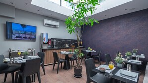 Un comedor moderno con sillas y mesas negras, una planta en maceta y un cuadro grande en la pared.