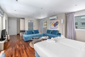 A modern hotel room with a large bed, two blue sofas, a desk with a computer, and a TV. - Aeolos Luxury Suites (Athens)