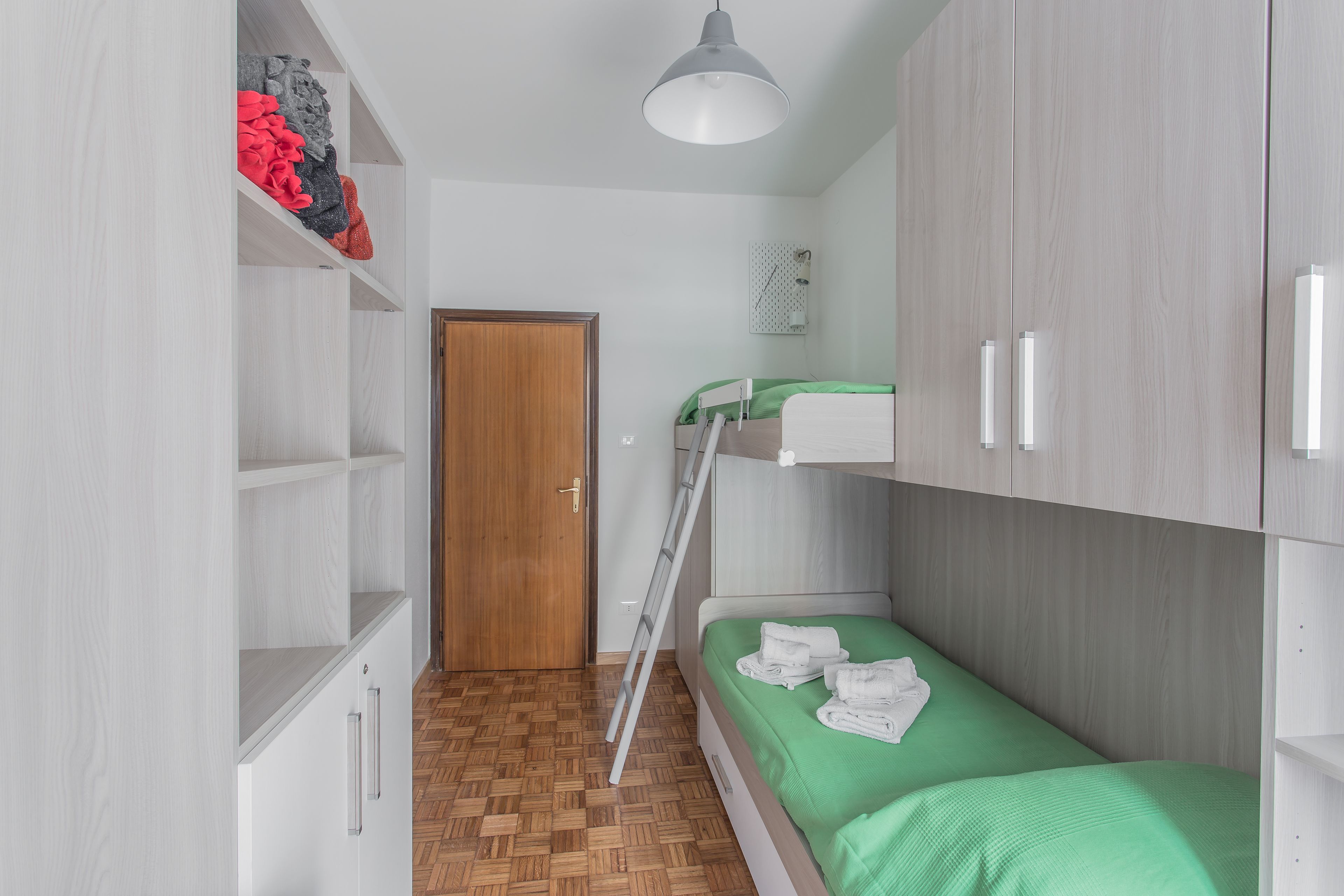 A small, neatly organized room with a bunk bed, a ladder, a wardrobe, and a shelf with folded clothes.
