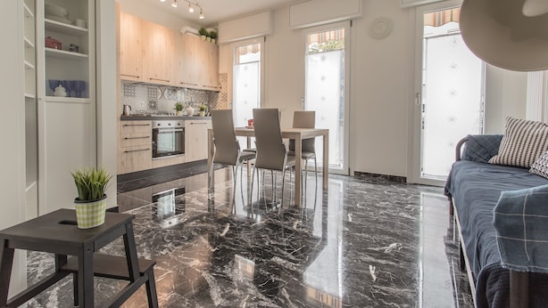 A modern kitchen with wooden cabinets, a dining area with chairs, a marble floor, and a bed with a blue blanket. - Padova - Pierobon 18 (Padova)