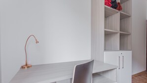 A minimalist workspace with a desk, chair, and a white shelving unit with a few items on top. - Padova - Pierobon 18 (Padova)
