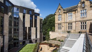 A courtyard with a modern building and a traditional stone building, both with multiple windows and a grassy area with a bench. - Popup Durham (Durham)