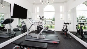 A gym with treadmills, elliptical machines, and stationary bikes, large mirrors, and a TV. - Popup Durham (Durham)
