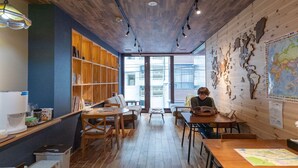 A cozy library with wooden bookshelves, a large world map, and a person reading. - HOSTEL PAQ tokushima - Hostel (Tokushima)