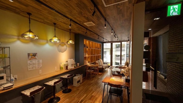 A modern bar area with wooden flooring, pendant lighting, and a seating area with tables and chairs. - HOSTEL PAQ tokushima - Hostel (Tokushima)