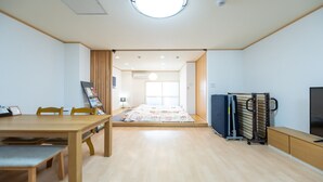 A modern, well-lit room with a wooden dining table, a bed with a colorful quilt, a TV, and a storage unit. - HOSTEL PAQ tokushima - Hostel (Tokushima)