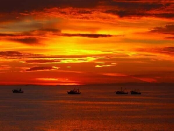 A sunset over a calm sea with three boats.