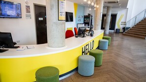 Un espace d’accueil doté d’un comptoir jaune, de plusieurs options d’assises, d’un escalier et d’un téléviseur diffusant des images d’un événement étudiant.