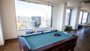 Une table de billard dans une pièce dotée de grandes fenêtres donnant sur un paysage urbain.
