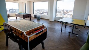 Un espace de loisirs intérieur moderne, doté d’un baby-foot, d’une table de ping-pong et d’un billard, et offrant de grandes fenêtres avec vue sur la ville.