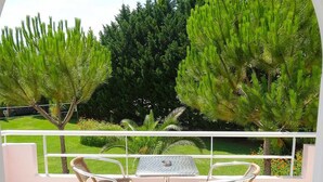 A balcony with a table and two wicker chairs, overlooking a well-manicured lawn and trees. - Chroma Studios (Istiaia-Aidipsos)