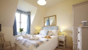 Une chambre à coucher avec un lit, des tables de chevet, une armoire, une fenêtre avec des rideaux et un miroir au mur.