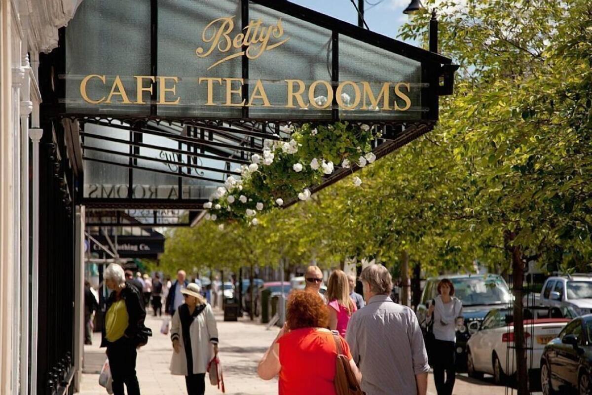 Una cafetería con un letrero que dice "Betty's Cafe Tea Rooms" y un área de estar al aire libre cubierta con flores blancas.