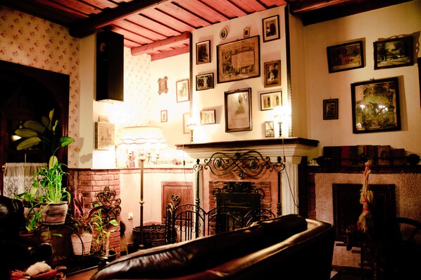 A cozy living room with a fireplace, a sofa, and various framed pictures on the walls. - Aranygombos Fogadó (Telkibánya)