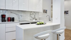A modern kitchen with white cabinetry, a marble backsplash, and a central island with bar stools. - Luxurious Spacious Apt next  Hilton Area (Athens)