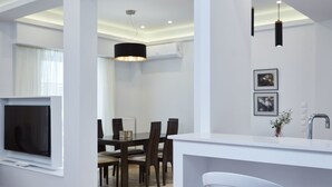 A modern living room with a TV, dining area, and kitchen counter. - Luxurious Spacious Apt next  Hilton Area (Athens)