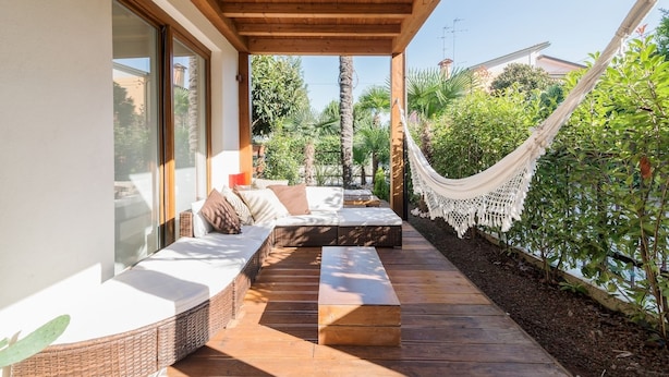 A covered outdoor seating area with a hammock, wooden deck, and a view of greenery and buildings. - Padova - Via Ancillotto 11B (Padova)