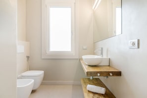 A modern bathroom with a toilet, a sink with a wooden countertop, a mirror, and a window.