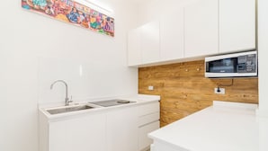 A modern kitchen with white cabinetry, a wooden accent wall, a stainless steel sink, and a microwave. - Padova - Via Ancillotto 11B (Padova)