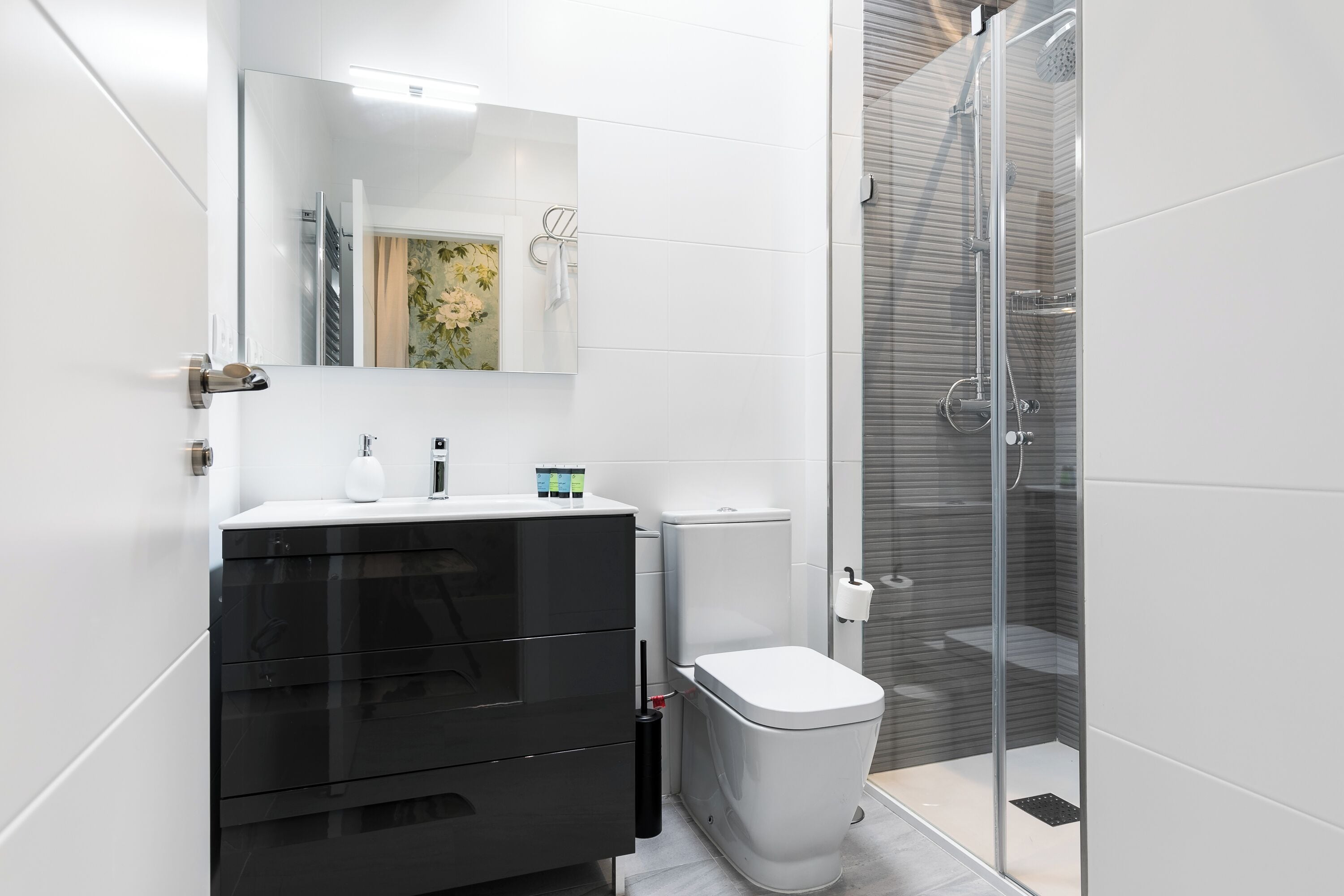 Un baño moderno con tocador negro, inodoro blanco y zona de ducha con mampara de vidrio.