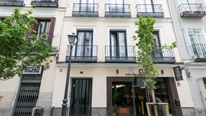 A building with multiple balconies, a storefront with a sign, and a tree in front. - Feelathome San Marcos Apartments (Madrid)