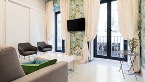 A modern living room with a sofa, two armchairs, a TV mounted on the wall, and a balcony with curtains. - Feelathome San Marcos Apartments (Madrid)