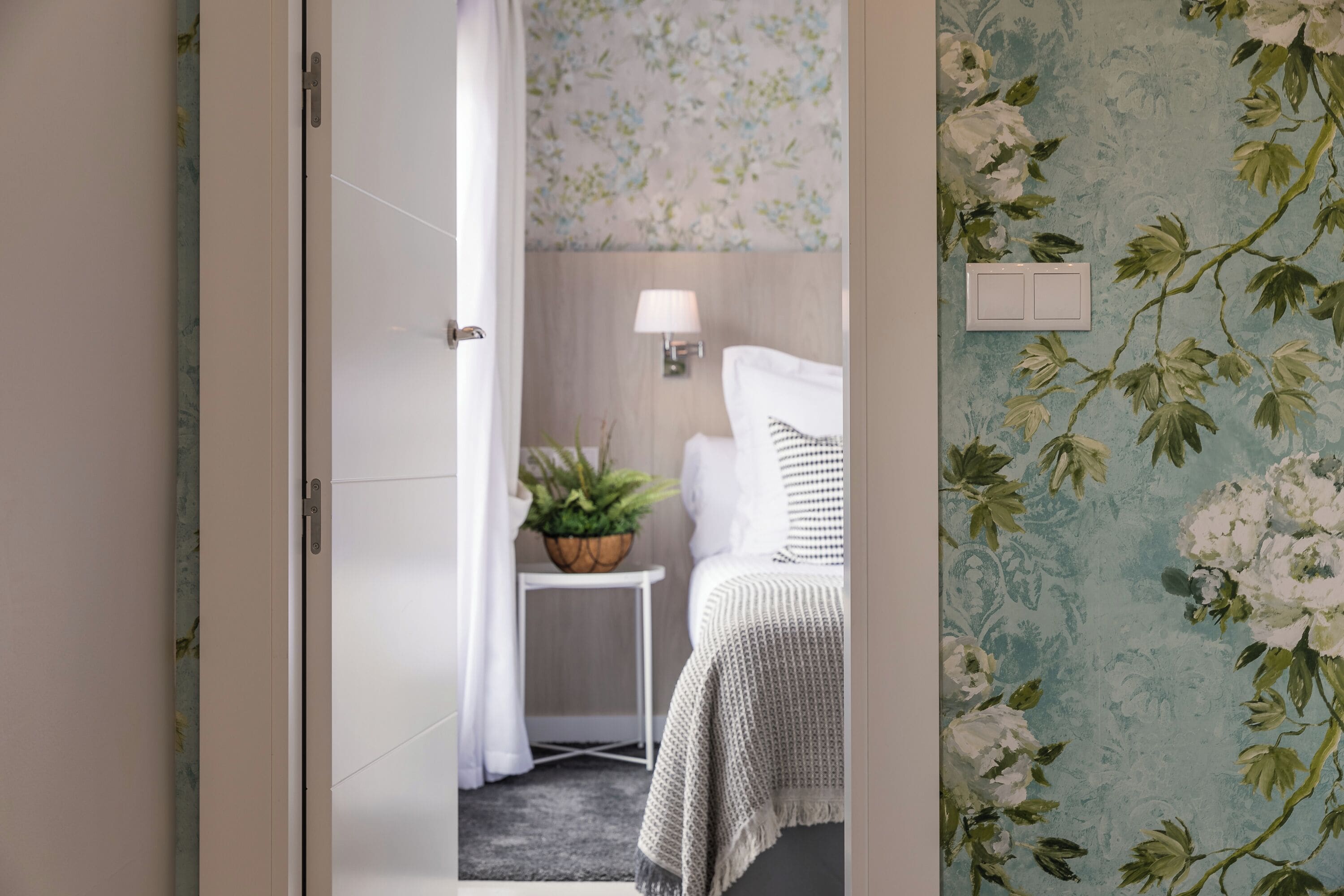 Un dormitorio con una cama, una mesita de noche con una lámpara y una planta en maceta.