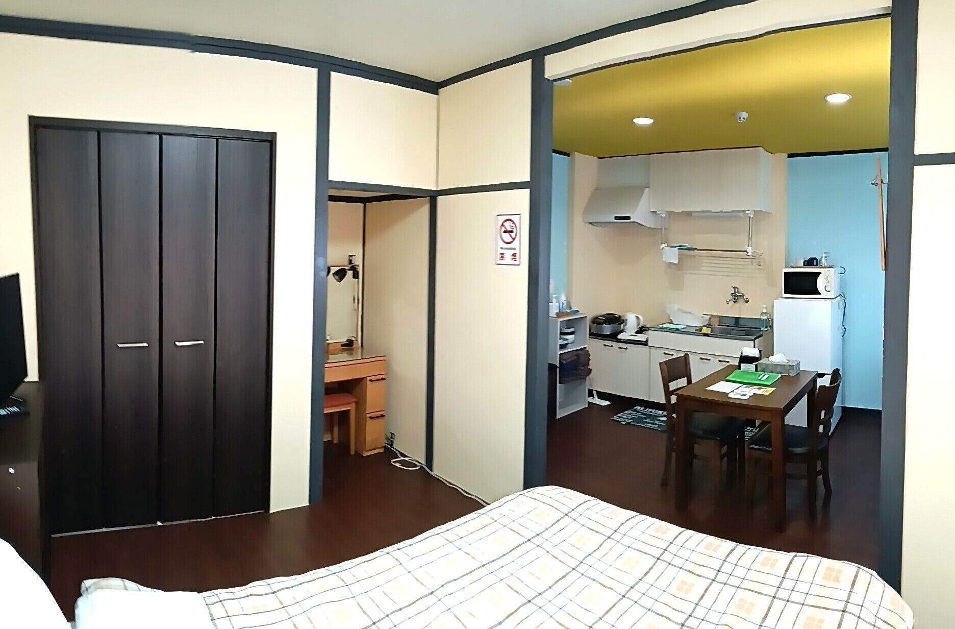 A hotel room with a bed, a desk, a kitchenette, and a wardrobe.