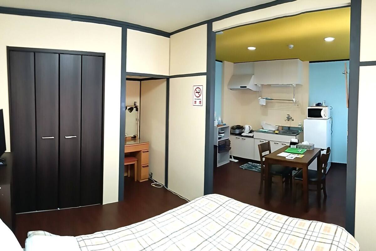 Quarto de hotel com cama, escrivaninha, cozinha compacta e guarda-roupa.
