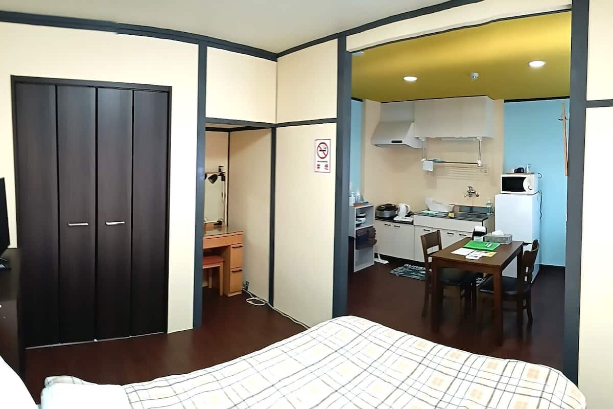 Quarto de hotel com cama, escrivaninha, cozinha compacta e guarda-roupa.