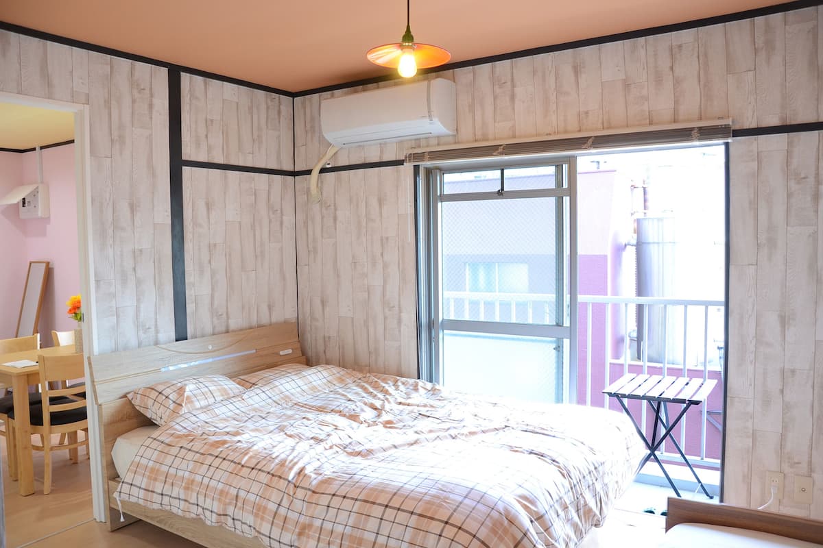 Quarto com cama, escrivaninha e janela com vista para uma varanda.