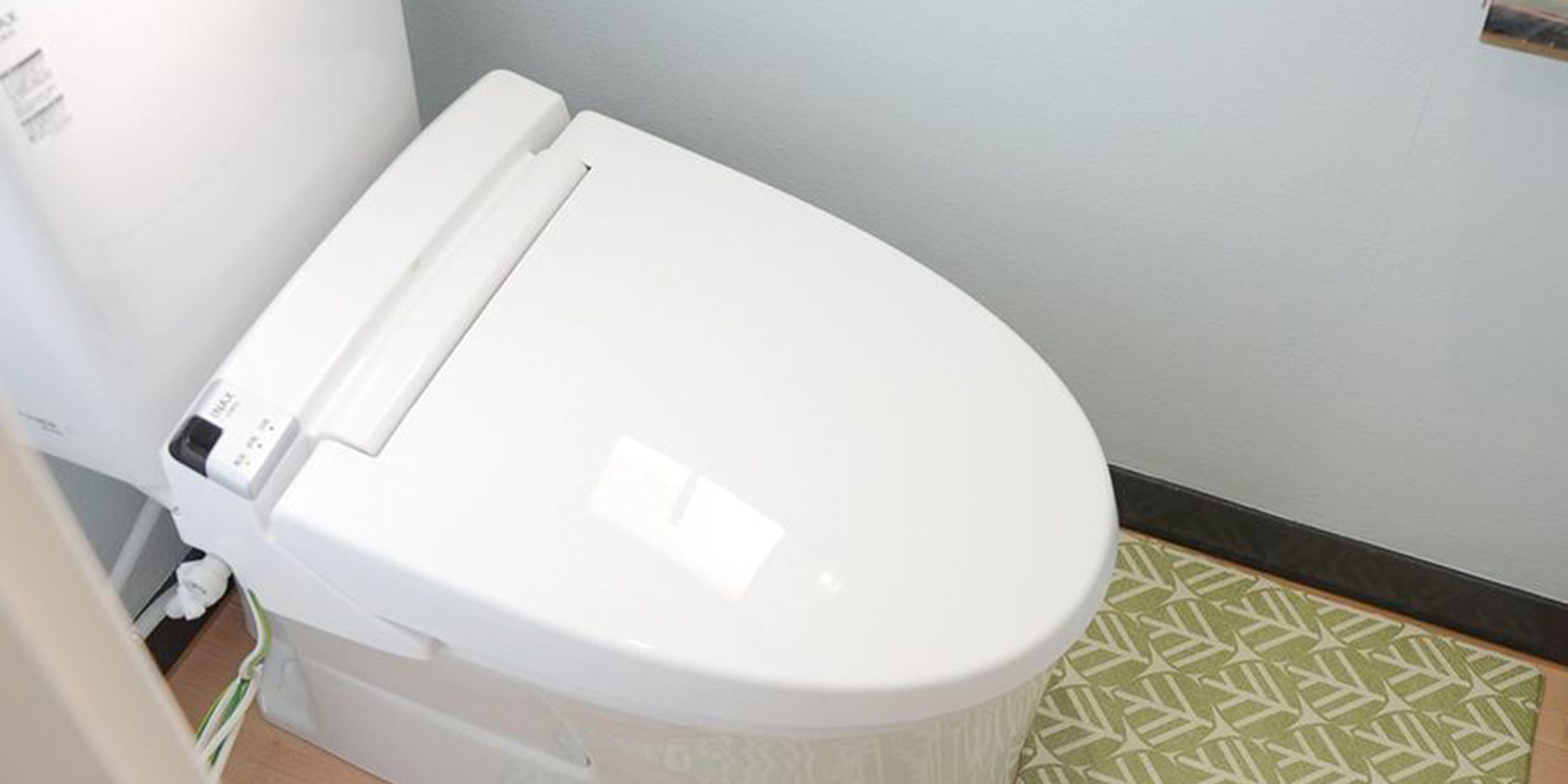 A white toilet in a bathroom with a patterned floor mat.