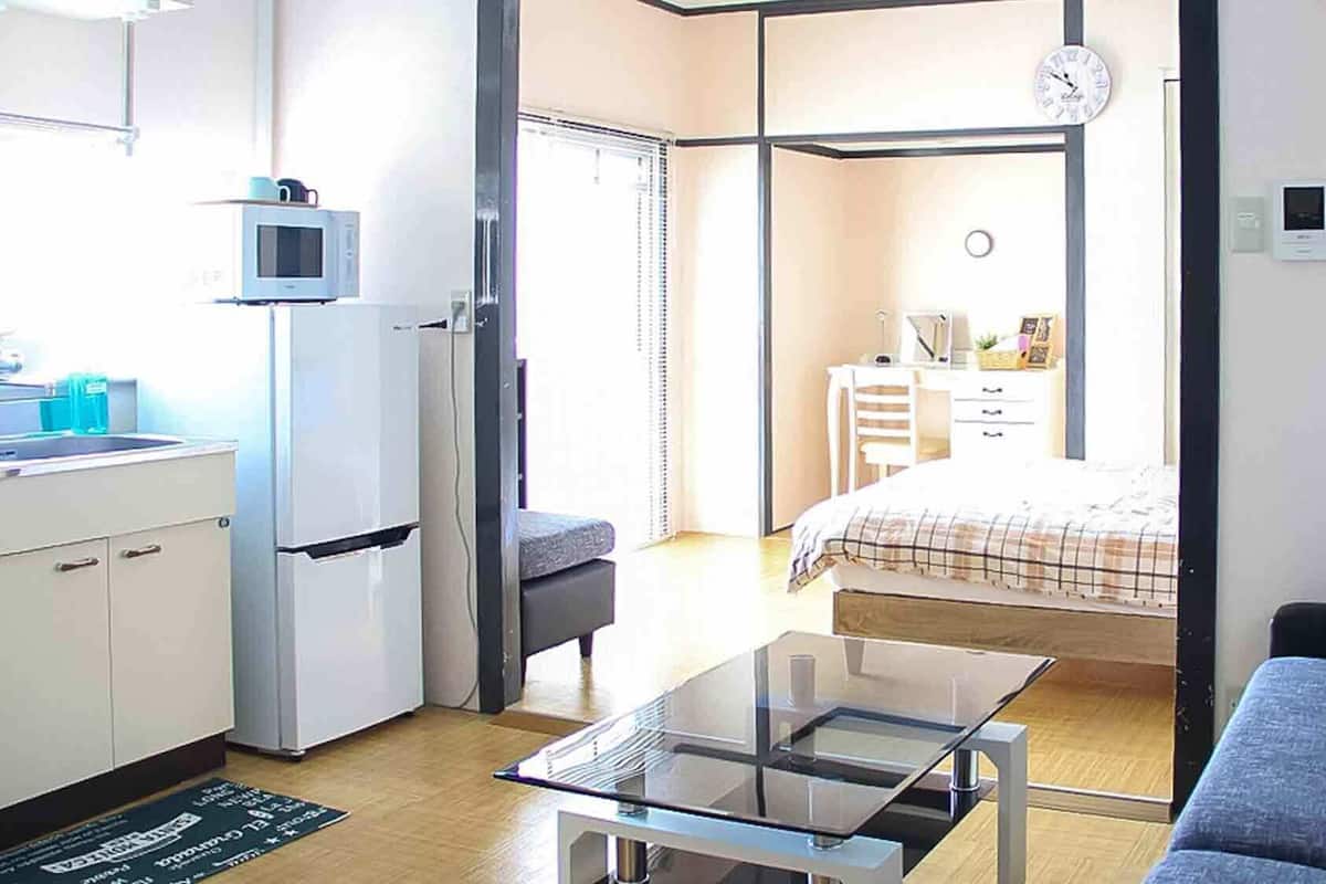 A compact room with a kitchenette, a bed, a sofa, and a glass table.