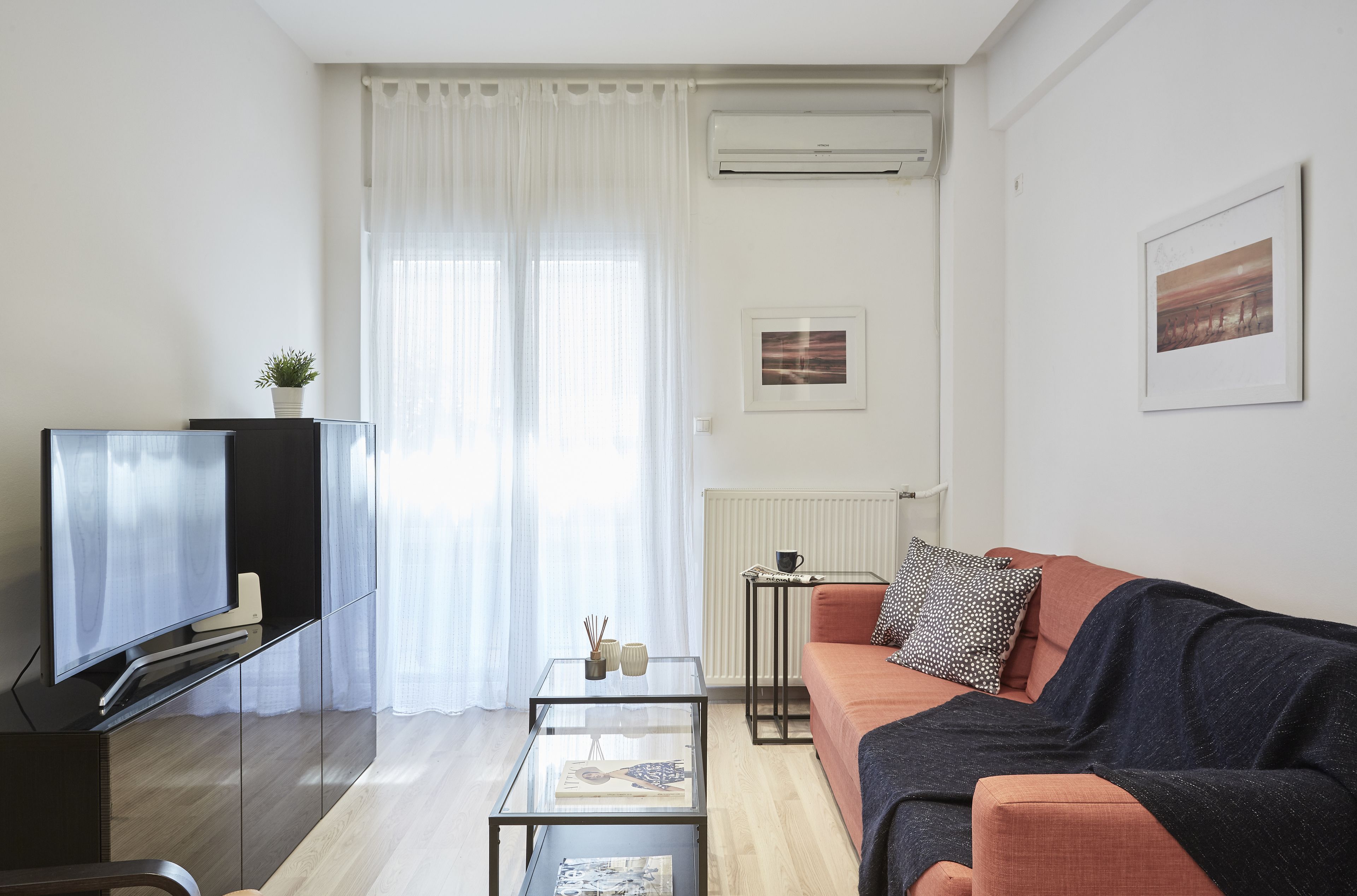 A modern living room with a flat-screen TV, glass coffee table, and a sofa with a throw blanket.